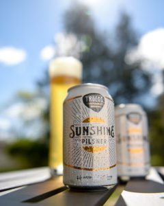 Sunshine Pilsner cans and glass outdoors.
